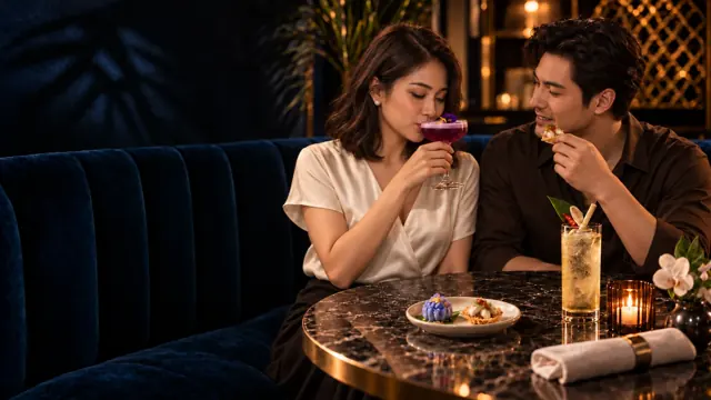 A couple enjoying a purple cocktail and Thai small plates in the same navy booth.